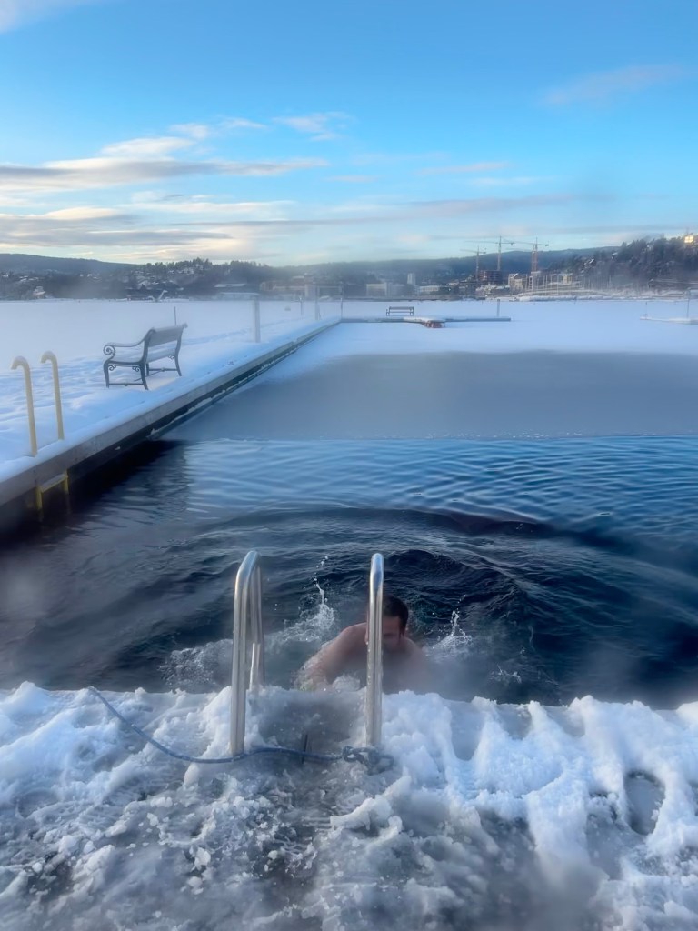 Person emerging from icy water at a frozen outdoor swimming spot in Norway.