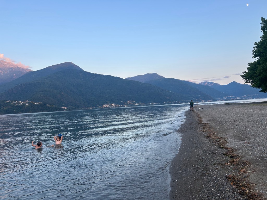 People swimming in Lake Como at sunset with mountains and shoreline in the background, northern Italy