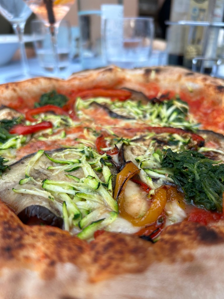Vegetable pizza served outdoors at a restaurant near Lake Garda, Italy, with drinks and table setting
